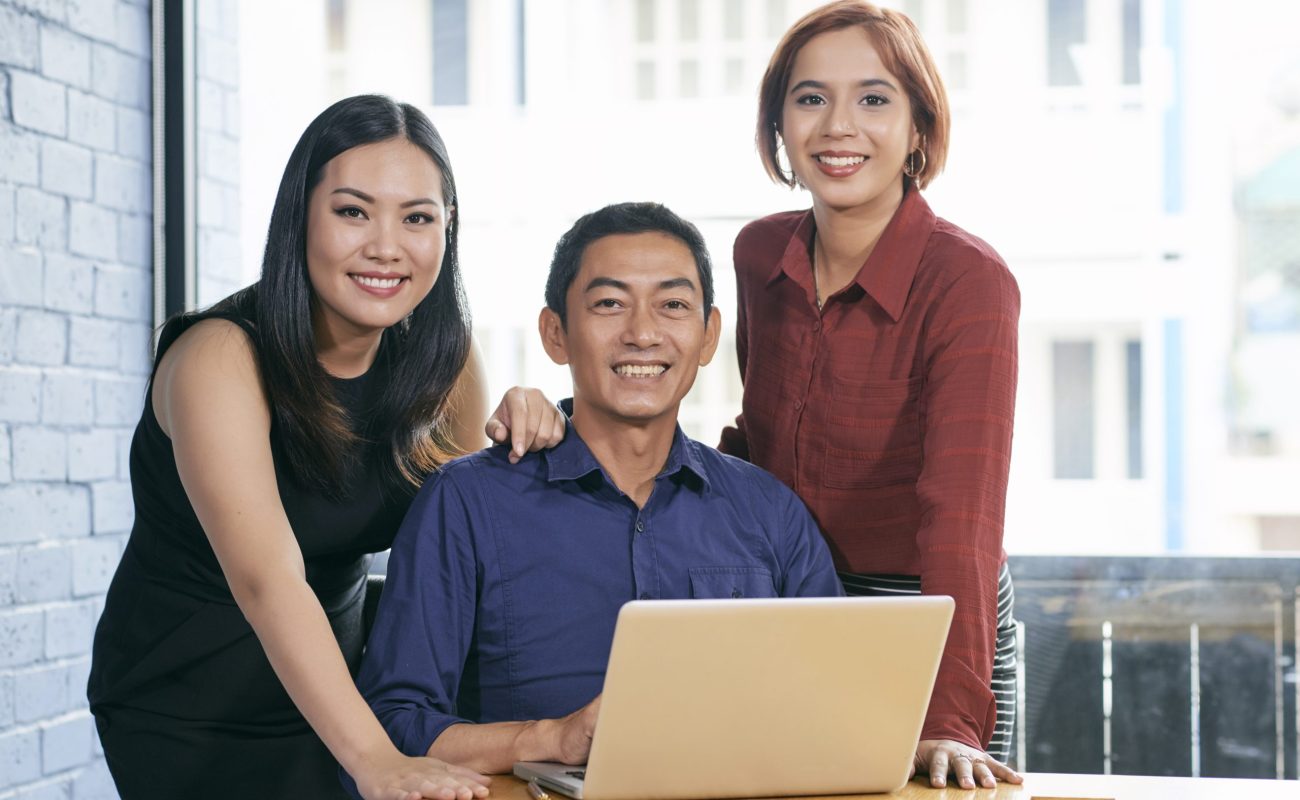 Cheerful business team Happy successful Asian business team gathered at laptop in office