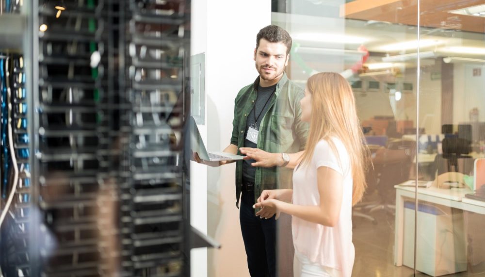 two-business-people-standing-server-room-with-laptop-discussing